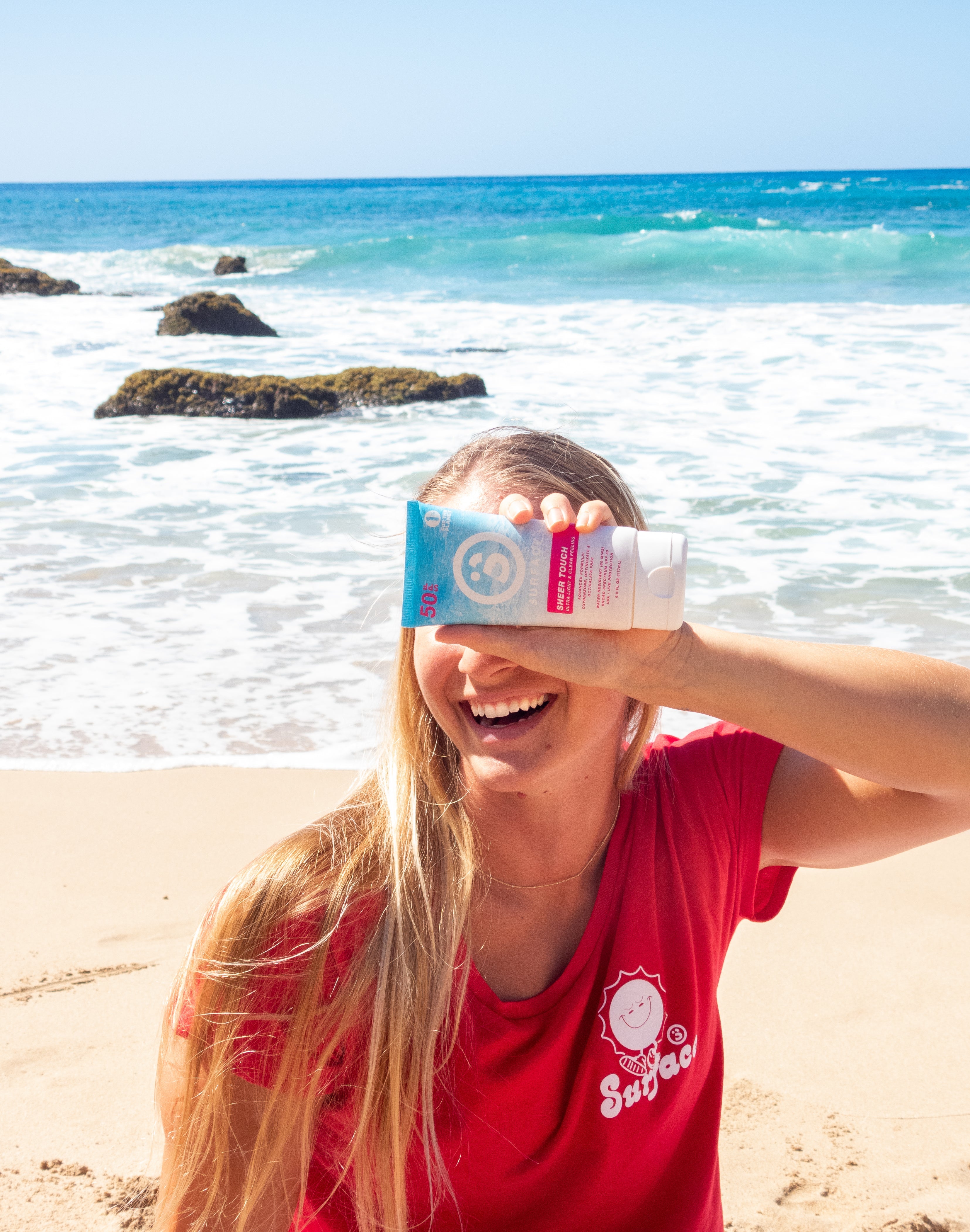 Blonde Girl on Beach Smiling Holding Sheer Touch Sunscreen