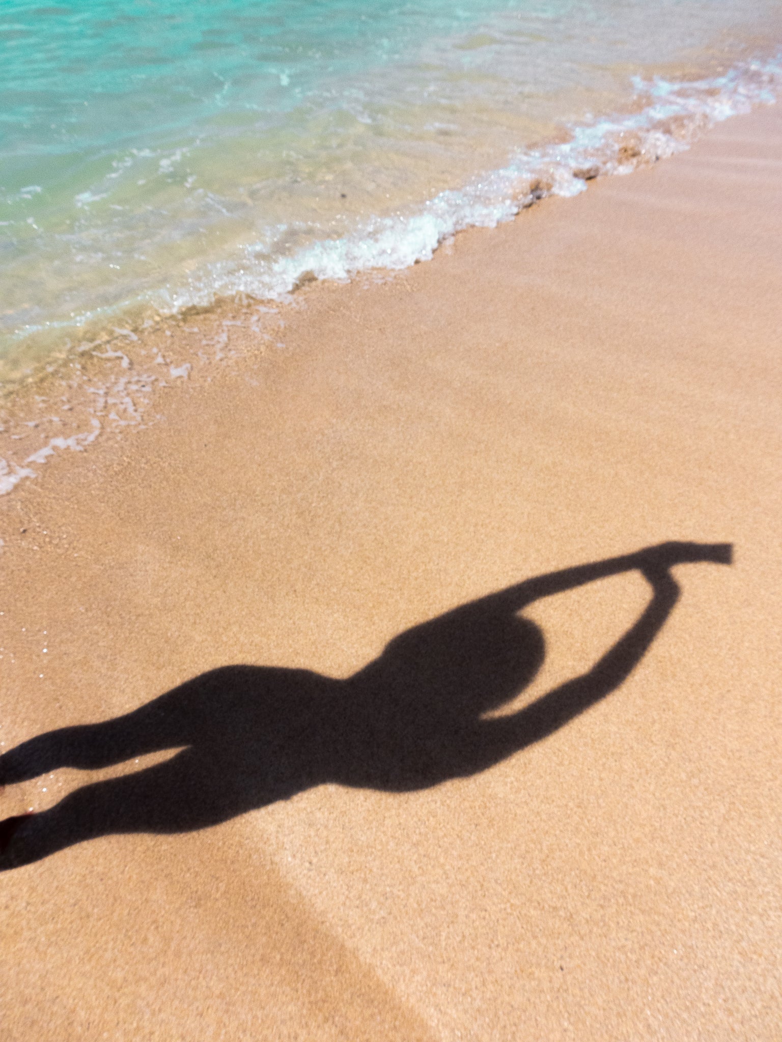 Shadow of girl stretching arms to the sky on a sandy ocean beach