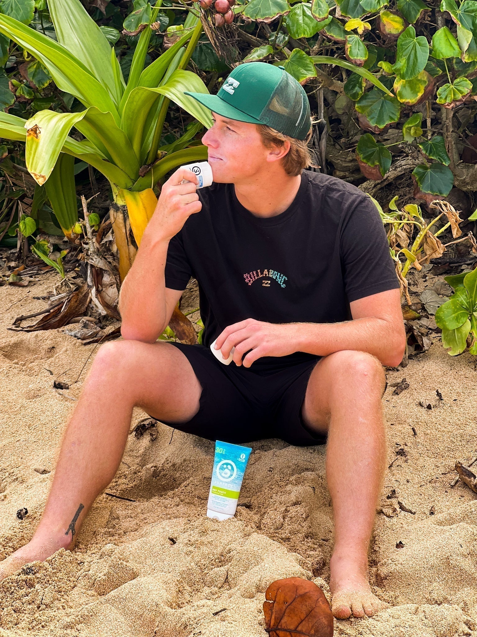 Man putting sunscreen on face while sitting on a tropical beach before going swimming
