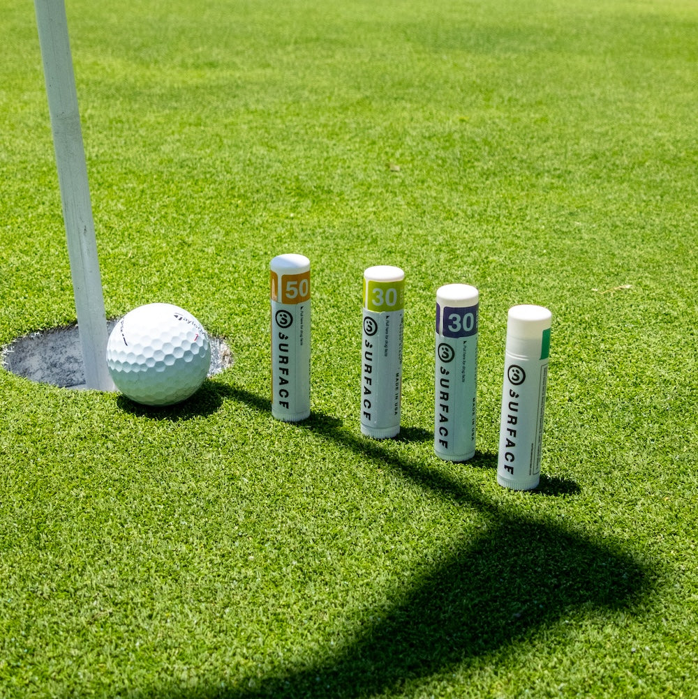 Surface Natural Moisturizing Lipbalms lined up next to golf cup