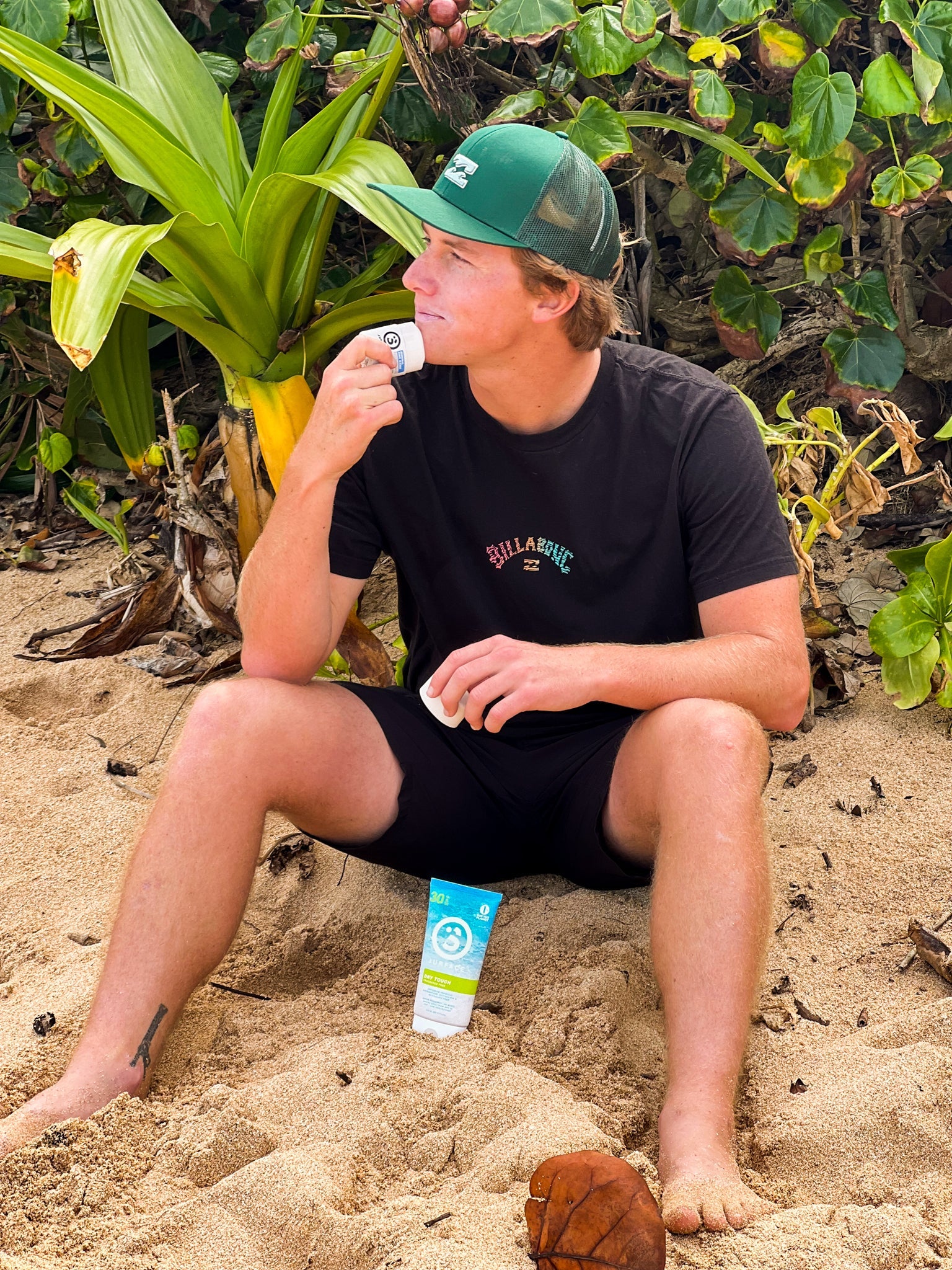 Man putting sunscreen on face while sitting on a tropical beach before going swimming